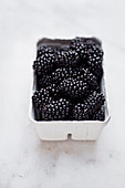 A punnet of fresh blackberries on a marble surface