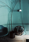 Pendant lamp with long cable, convex mirror, little tree and shell chair in front of petrol-coloured wall