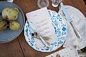 Blau-weißes Gedeck mit Menükarte und Silberbesteck auf Holztisch