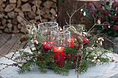 Windlichter im Drahtkorb, weihnachtlich dekoriert mit Zweigen von Tanne, Lärche, Ahorn und rotem Christbaumschmuck