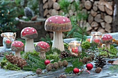 Forest look with toadstools made of wood, fir branches, pinecones, red ornaments, and votives