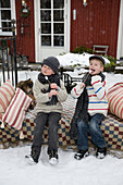 Children with roasting marshmallows on skewers on a snowy terrace