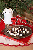 Marshmallows dipped in chocolate, cups, and a pitcher on a red tray