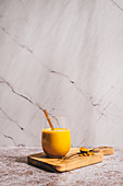 Goldene Milch im Glas mit Glastrinkhalm auf Holzbrett