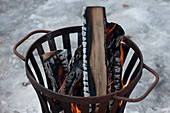 Feuerkorb mit brennenden Holzscheiten im Schnee