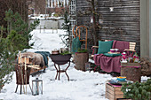 Terrasse für die Winterparty: Töpfe mit heißem Punsch auf dem Grill, Feuerkorb, Bank und Brennholzregal mit Fell, Decke, und Kissen als Sitzplätze, Stockbrot an Feuerkorb gelehnt