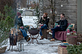 Freunde sitzen gemütlich auf der Terrasse mit Grill und Feuerkorb