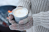 Frau hält Tasse mit heißem Cappuccino mit Handschuhen