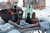 Holzkiste mit Bierflaschen und Wasserflaschen, Feuerschale im Hintergrund