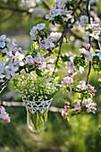 Bouquet of lilies of the valley in a hanging vase hung on a blossoming apple tree