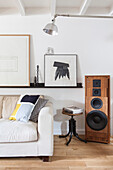 White sofa, with a shelf above it with modern art, stool, and speakers in a loft