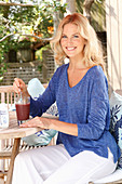 Blonde Frau in blauem Shirt und weißer Hose mit einem Drink