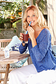 Blonde Frau in blauem Shirt und weißer Hose mit einem Drink