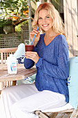 A blonde woman wearing a blue shirt and white trousers with a drink