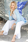 A blonde woman wearing a white top and a light blue cardigan sitting in a hammock