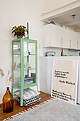 Green glass cabinet, balloon bottle, pillows, and large-format quotation poster in the room