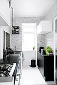 Narrow kitchen with black and white furniture, white floor and white-painted brick wall