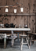 Antike Gläser und schwarzes Geschirr auf Tisch vor rustikaler Bretterwand