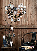 Alte Fotos in Herzform arrangiert an rustikaler Bretterwand, darunter Stuhl und Beistelltisch