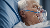 Man wearing oxygen mask in hospital bed