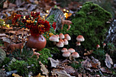 Woodland arrangement of fungi, moss, animal figurines and vase of chrysanthemums and pyracantha berries