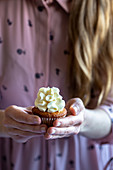 Woman with blond hair and pink dress holding a cupcake with white frosting