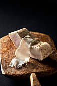 A piece and a thin slice of lardo on a wooden board