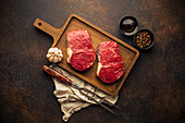 Two raw beef steaks on wooden cutting board