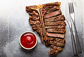 Sliced grilled medium rare T-bone beef steak with ketchup