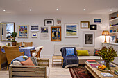 Bildergalerie an der Wand in offenem Wohnzimmer mit Sessel aus Holz, Sofa und Essbereich