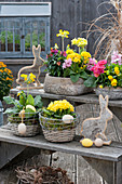 Arrangement on flower stairs: bowls and baskets with primroses, cowslip, wallflower 'Winter Orchid', horned violets and hyacinths, Easter bunnies and Easter eggs, a wreath of larch cones