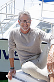 A grey-haired man at a harbour wearing a light-coloured outfit
