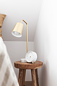 Lamp and alarm clock on solid wooden stool used as bedside table