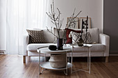 Pale sofa with scatter cushions and round coffee table decorated with branches