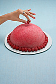 Woman hand deposing a raspberry on a pink pastry dome