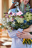 Frau mit Blumenstrauß aus Nelke, Schleierkraut, Knorpelmöhre, Ehrenpreis, Kugeldistel, Sterndolde und Eukalyptus