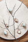 Liegende Osterdeko mit Zweig, Ostereiern, Rosenblüte, Narzissenblüte und Waxflower
