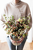 Woman holding vase of roses, waxflowers, St. John's wort with white berries and willow catkins