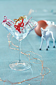 Empty cocktail glass on pale blue tablecloth with ice cube gift ornaments reindeer and copper light garland