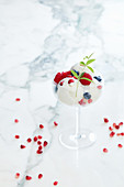 White ice cup with Raspberry pomegranate grains blackcurrant verbena leaves on white marble background inside