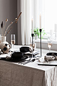 Gedeckter Tisch mit Leinentischdecke und schwarzem Geschirr