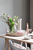 Frühlingsstrauß mit Tulpen und pastellrosa Kerzen auf Tisch