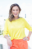 A dark-blonde woman wearing a yellow blouse and orange shorts