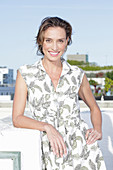 A dark-blonde woman wearing a fern-patterned sleeveless dress