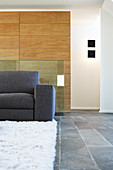 Graues Sofa auf weißem Teppich vor Eichenholz-Verkleidung im Wohnzimmer