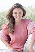 A young, long-haired woman wearing a pink blouse and light trousers