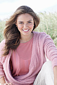 A young, long-haired woman wearing a pink blouse and a pink wrap-around jumper