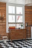 Antique dresser in front of a window and potty in a bathroom with black and white floor tiles