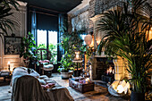 Überdecktes Sofa vor Kamin mit Feuer in eklektischem Wohnraum voller Pflanzen