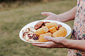 Man holding plate with grilled corn